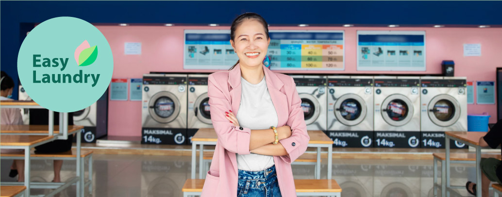 A woman wearing pink trouser standing infront of a laundry with multiple washing machines in the background