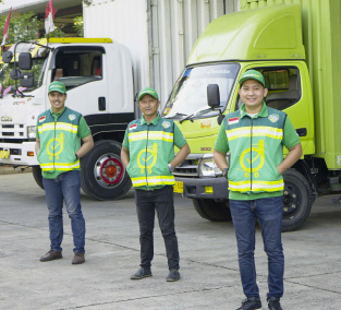 three drivers wearing green clothing standing side by side with their trucks on the background