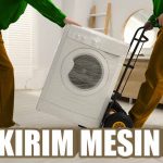 Dua orang mengangkat mesin cuci menggunakan troli.