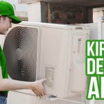 Seorang kurir Deliveree mengenakan seragam hijau sedang memasang unit AC besar di luar rumah, memastikan proses pengiriman berjalan dengan aman.