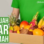Kurir Deliveree memegang kotak berisi berbagai buah segar dengan teks "Kirim Buah Segar ke Rumah".