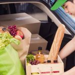 Kurir Deliveree sedang menata berbagai bahan makanan segar, seperti roti, sayuran, dan buah-buahan, ke dalam bagasi mobil untuk pengiriman.