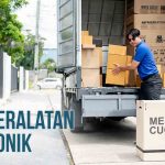 Pria memuat kotak peralatan elektronik ke dalam truk untuk pengiriman, dengan kotak bertuliskan "MESIN CUCI" di bagian depan truk.