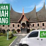 Mobil Deliveree berada di depan rumah adat Minangkabau dengan papan arah bertuliskan "Pindahan Rumah Padang."