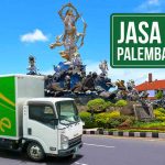 Truk Deliveree melintas di jalanan Denpasar Bali, dengan monumen Titi Banda terlihat di belakangnya. Terdapat tulisan “Jasa Kirim Palembang Bali” di pojok kanan atas.
