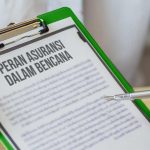 Gambar menunjukkan seseorang yang memegang papan klip dengan dokumen bertuliskan "Peran Asuransi dalam Bencana," sambil menunjukkan dengan pena.