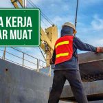Pekerja bongkar muat sedang mengangkat material dengan crane di pelabuhan.
