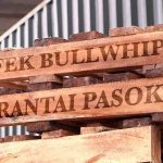 Pallet kayu dengan tulisan 'Efek Bullwhip pada Rantai Pasok' di atasnya di gudang