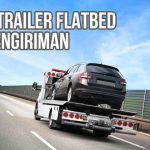 Trailer flatbed membawa mobil hitam di jalan tol dengan latar belakang langit biru cerah dan teks "Fungsi Trailer Flatbed pada Pengiriman".