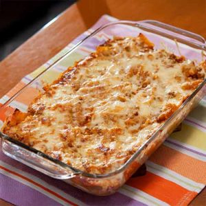 Wadah kaca berisi pasta panggang keju di atas kain berwarna-warni.