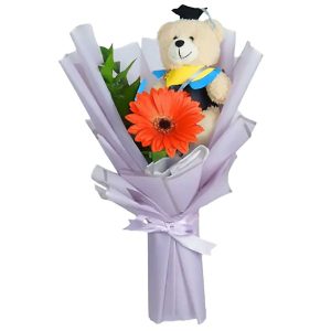 Buket wisuda berisi boneka ber-toga dan bunga gerbera oranye.