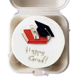 Kue bento dengan dekorasi topi toga dan buku bertuliskan "Happy Grad!"
