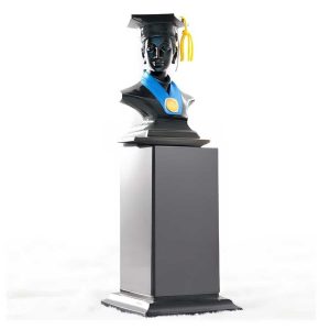 Patung piala wisuda dengan toga dan medali di atas pedestal hitam.